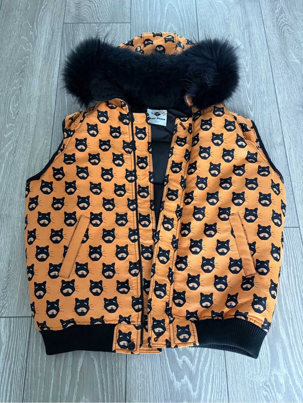 An orange and black cat-print winter puffer vest with a black faux-fur hooded